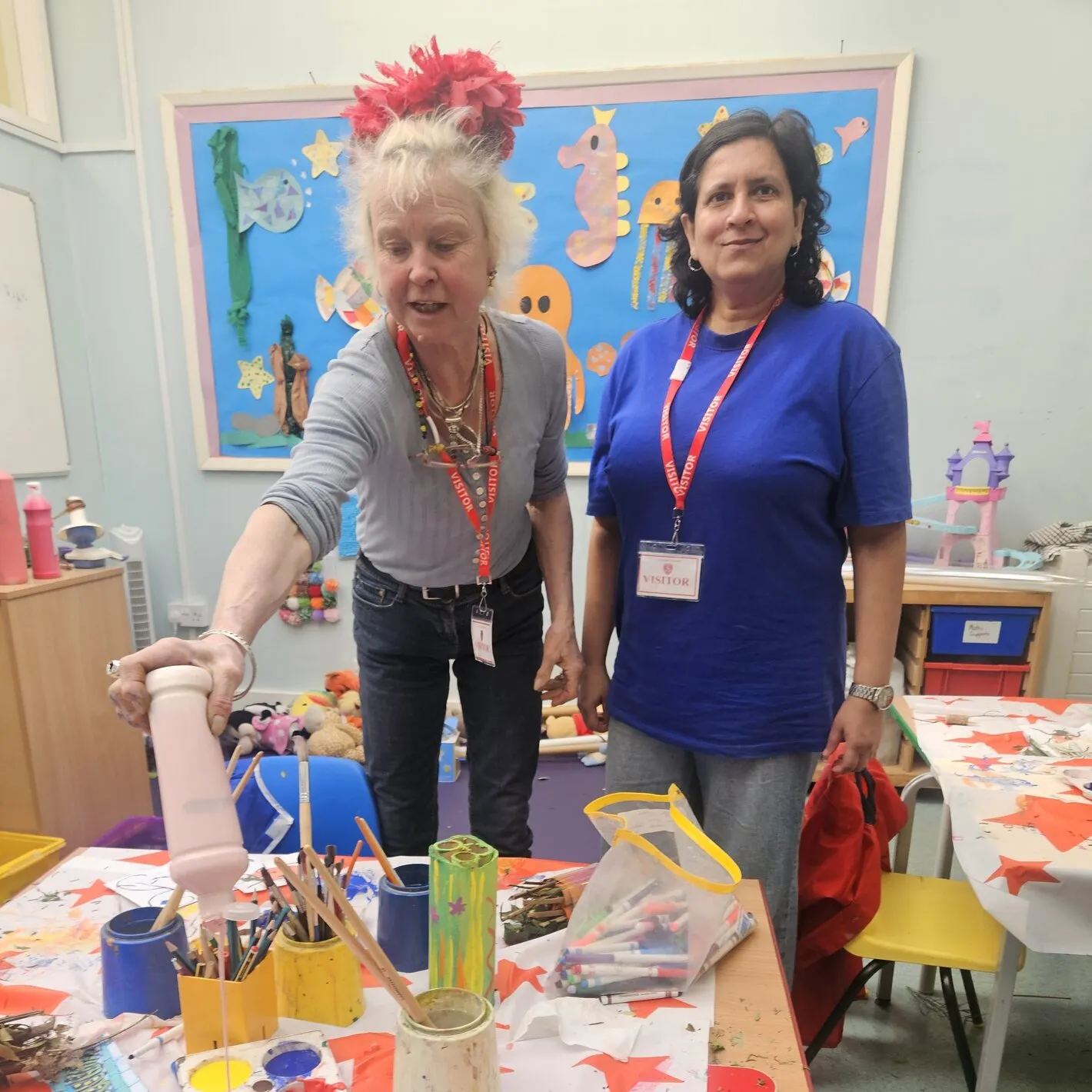 Two volunteers at a craft table in the store, sorting decorated card tubes and craft materials